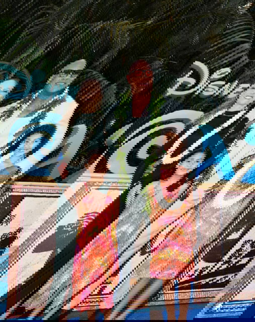 Дуэйн Джонсон вместе с супругой и двумя дочерьми в праздничных гирляндах на красной дорожке; семейный портрет на официальном мероприятии с тёплой атмосферой.