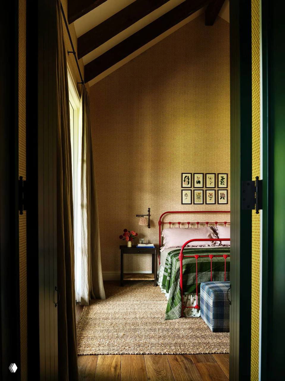 Узкая спальня с красной металлической кроватью, пледами и соломенным ковром: простые детали в стиле grandma‑chic и теплые деревянные полы горного дома.