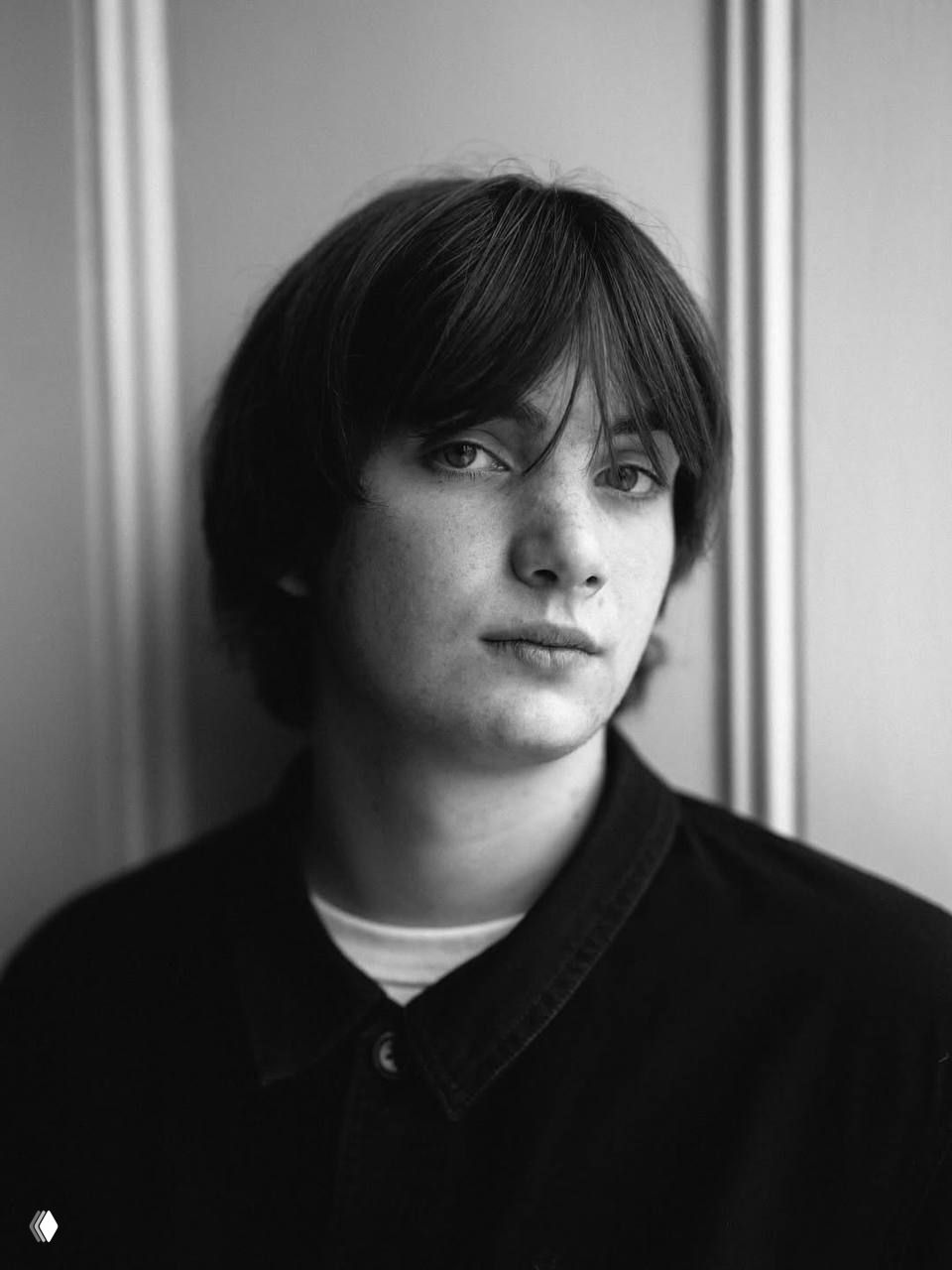 Чёрно‑белый портрет подростка крупным планом: короткая стрижка, нейтральный фон, серьёзное выражение лица в интерьере