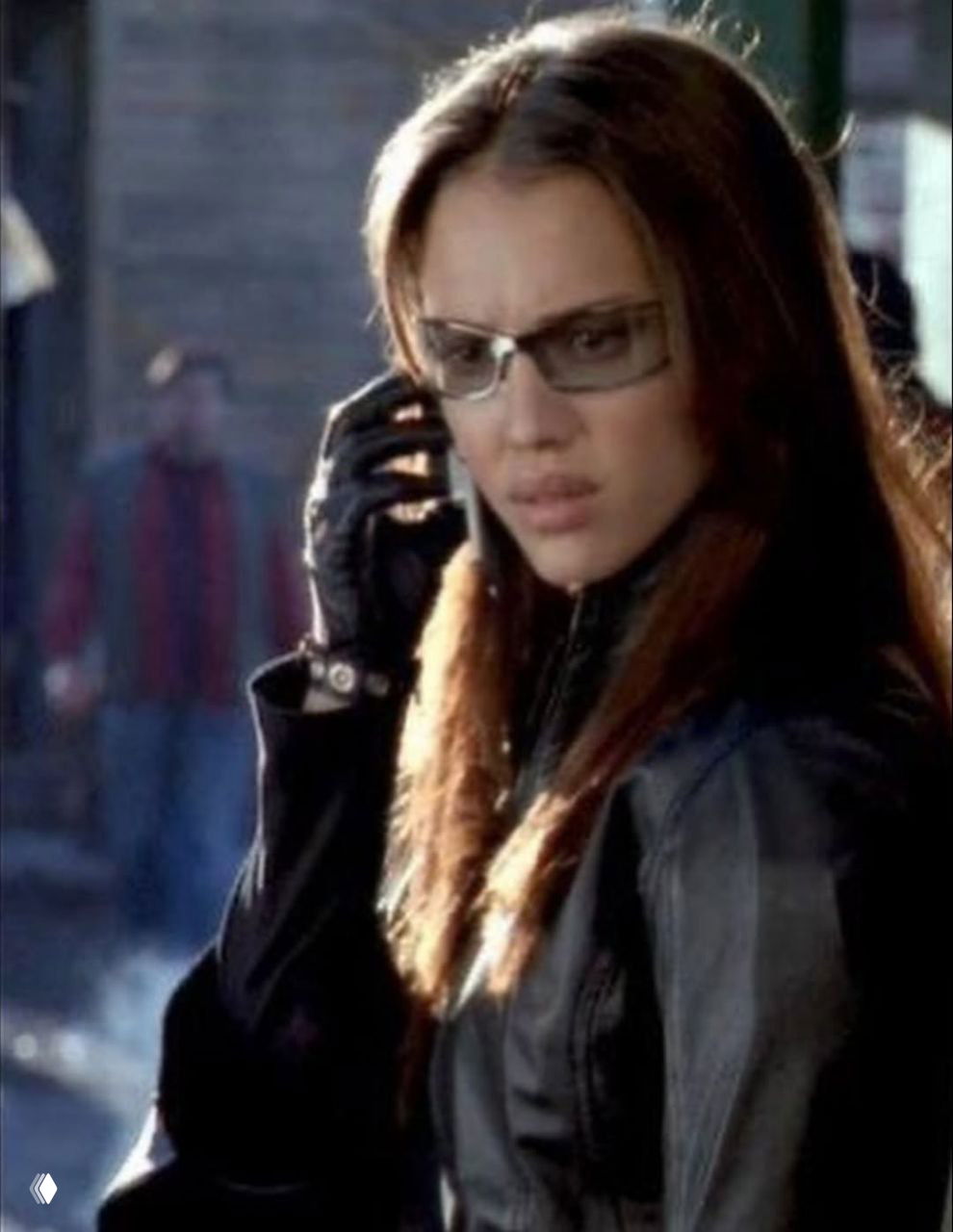 Кадр с Джессикой Альбой, говорящей по телефону в кожаной перчатке, напряженное выражение лица и атмосферный городской фон.