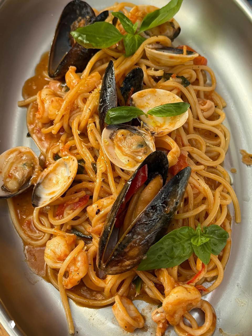 Тёплая городская сцена у большого колеса обозрения: Оля идёт по набережной мимо пальм и пешеходной зоны, рядом мужчина в шортах.