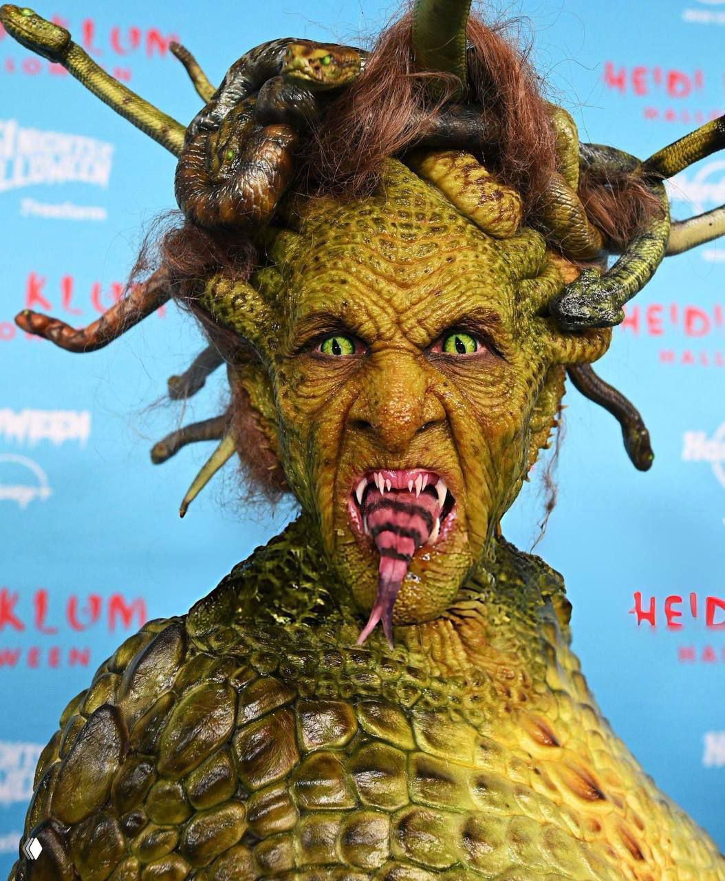 Крупный план Хайди Клум в костюме Медузы Горгоны: детализированная зелёная фактура лица, змеи вместо волос и разинутый рот с языком.