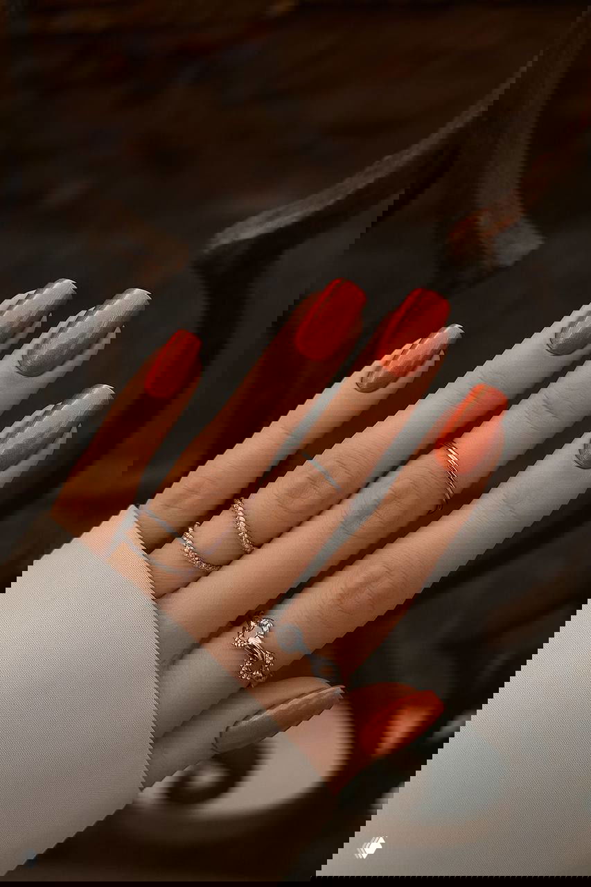 Оранжевый маникюр с легким металлическим сиянием и ровной формой ногтей на светлом фоне — яркий вариант для тёплого праздничного образа.