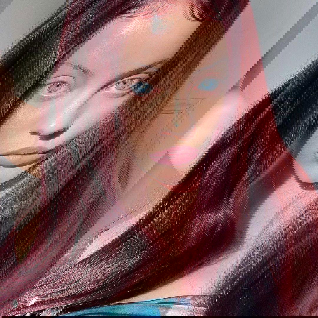 Портрет певицы Кати Кищук в крупном плане: лицо и бордовые волосы на светлом фоне, иллюстрация к материалу о её зависимости.