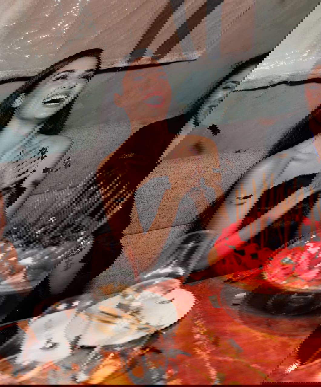 Ханде Эрчел смеётся и аплодирует за столом в окружении гостей, праздничная атмосфера и конфетти в кадре.