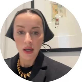 Тина Канделаки в видеоролике: крупный план лица, чёрный головной убор и золотое колье, нейтральный интерьер на заднем плане, лицо говорит в камеру