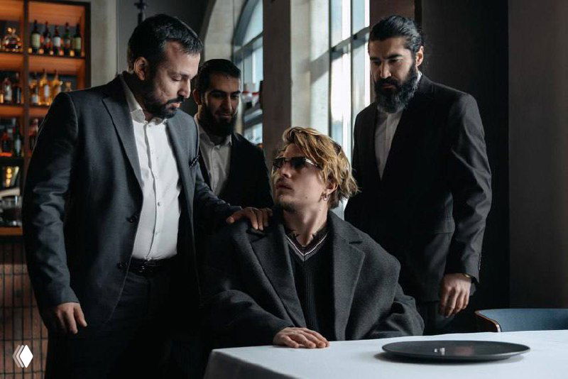 Искажённый групповой кадр: несколько человек у стола, присутствуют цифровые помехи и графические артефакты, фрагменты реквизита.