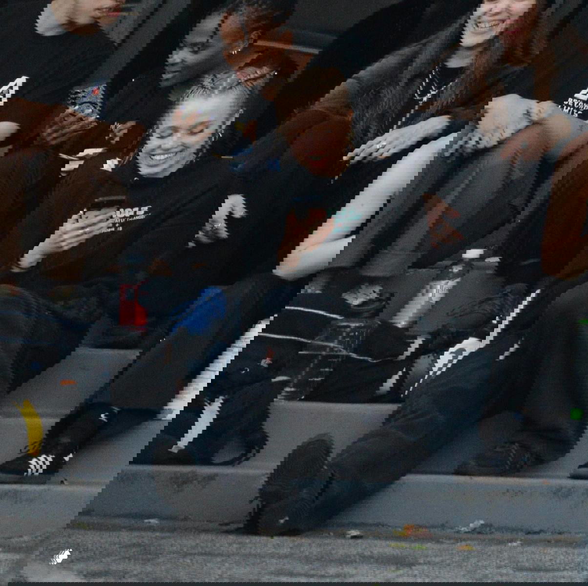 Подростки сидят на ступеньках и улыбаются, девушки смотрят в смартфоны — иллюстрация влияния соцсетей на детей.