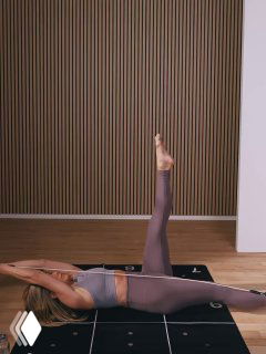 Женщина лежит на спине на коврике, поднимает прямую ногу вверх, выполняет упражнение на пресс и гибкость в студии с эспандером