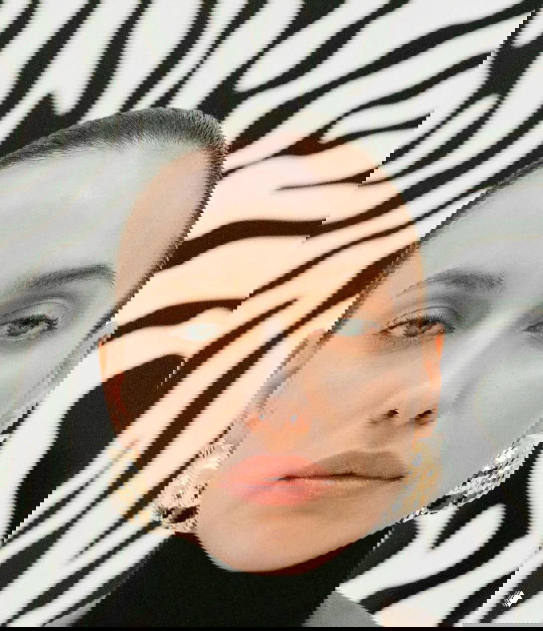 Крупный портрет на чёрно‑белом зебровом фоне: сдержанный макияж, массивные золотые серьги и минималистичная эстетика fashion‑съёмки.
