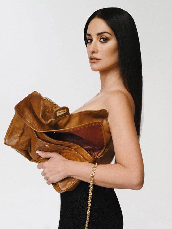 Портретный кадр в цвете: женщина в профиль держит большую кожаную сумку, лаконичный фон и элегантный макияж.