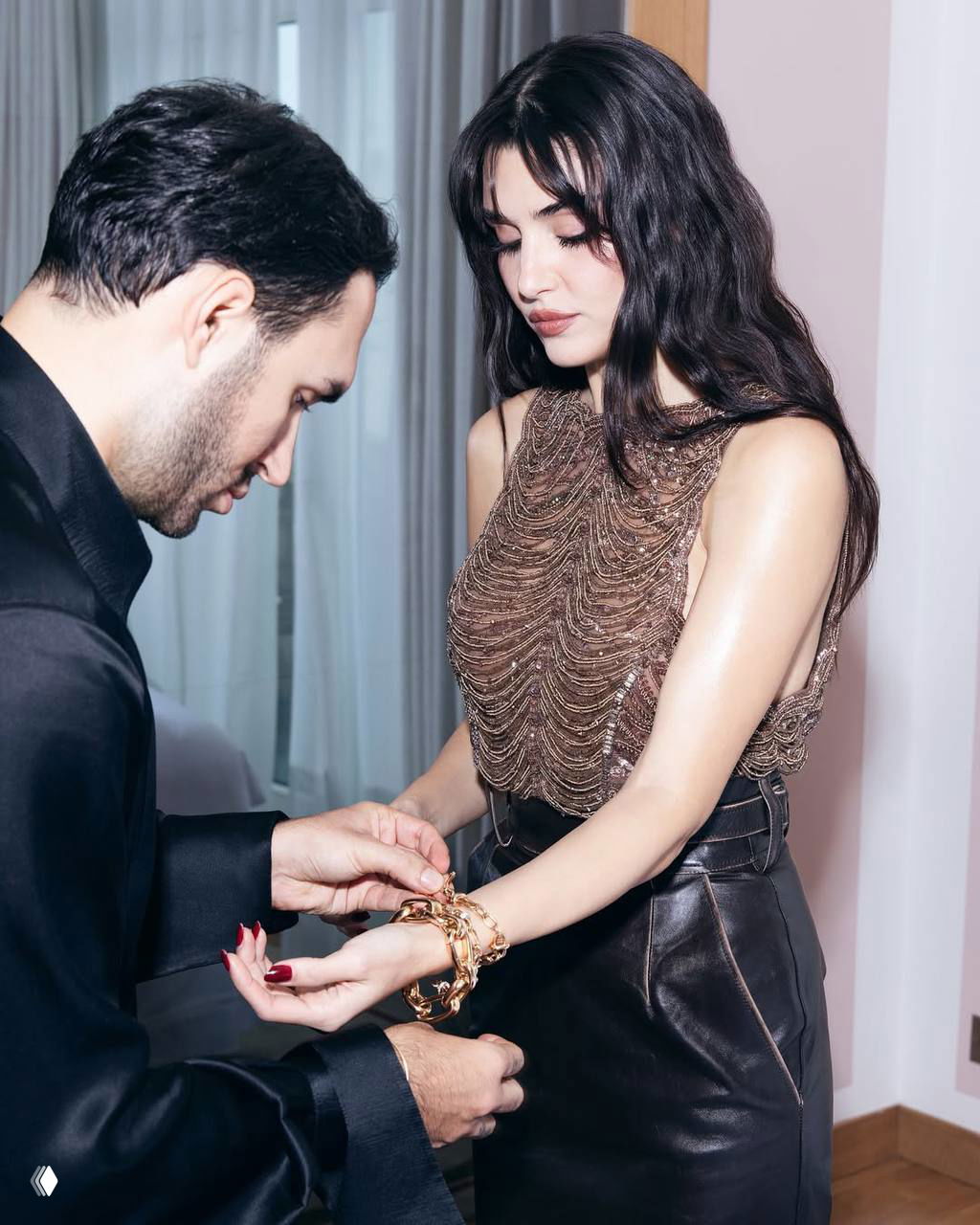 Кадр, где женщина осматривает браслет на руке, фотограф рядом помогает с украшением — закулисный момент подготовки к выходу.