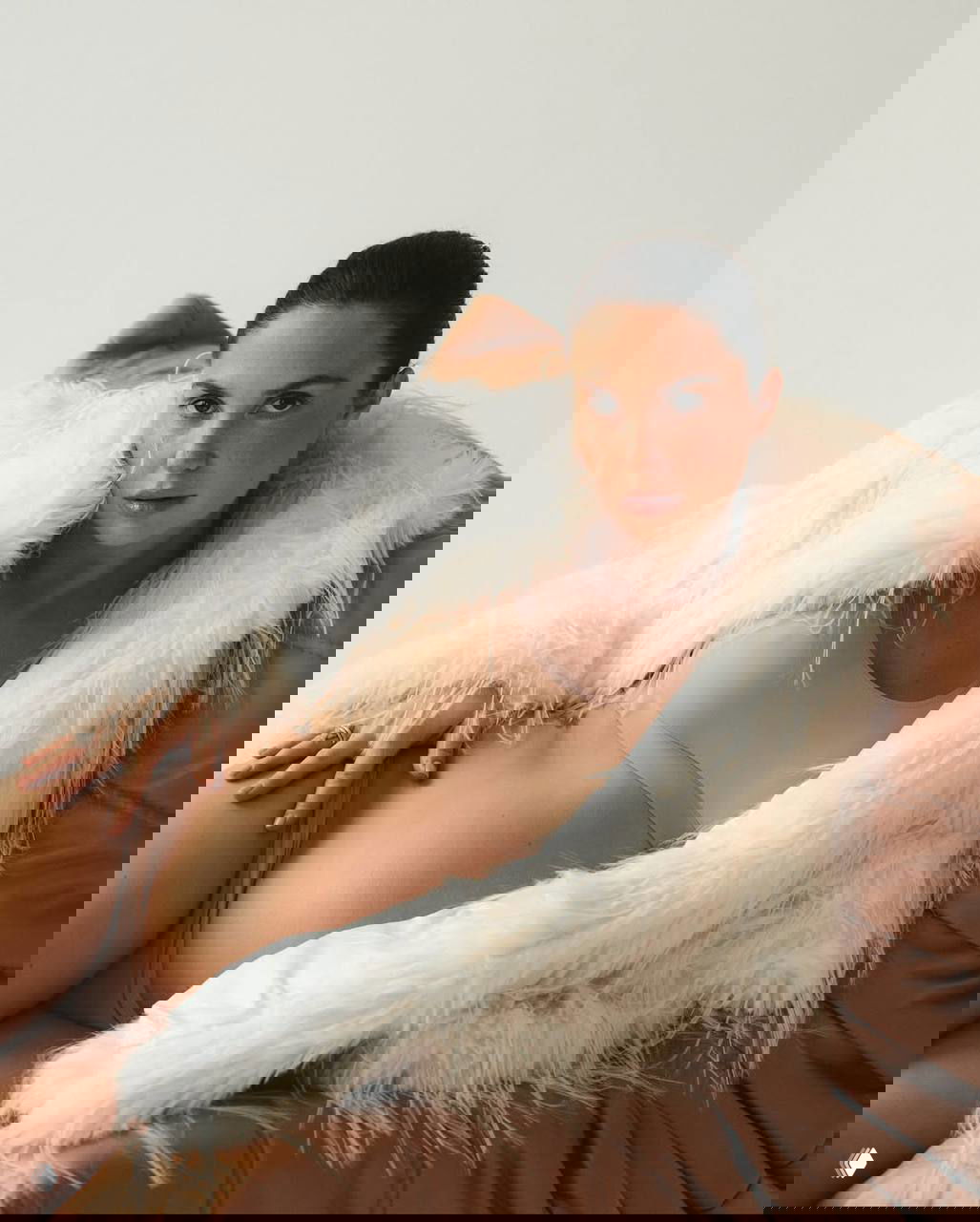 Крупный портрет беременной женщины в студии: бежевое бельё, белая пушистая шуба, естественный макияж и спокойный взгляд.