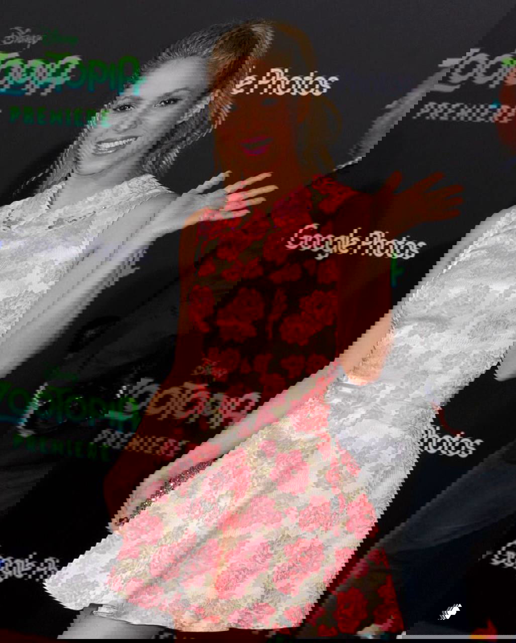 Женщина в цветастом платье на красной дорожке: растительный принт, светлая прическа и поза для пресс-фото в 2016-м стиле.