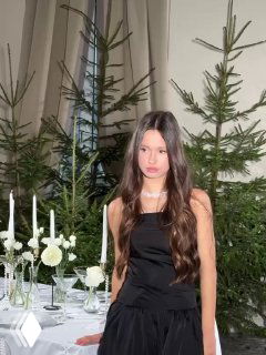 Девушка в черном платье у праздничного стола с белыми свечами и елочными ветками, оформленная как семейный фотокадр.