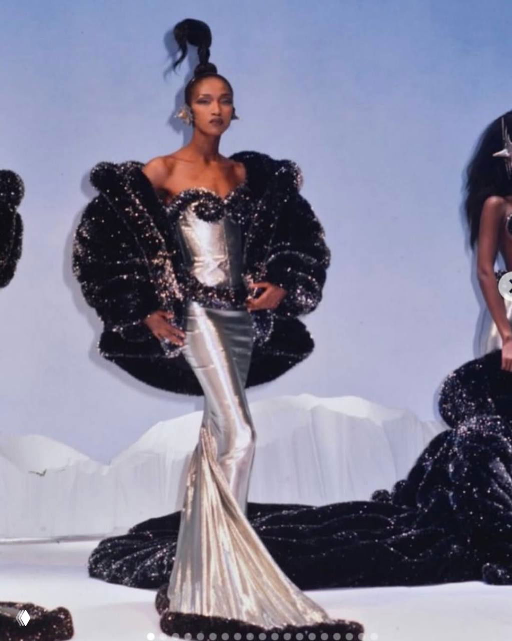 Архивный кадр 1986 года с показа Mugler: модель в серебристом корсетном платье и черном объемном аксессуаре.