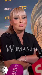 Крупный план Даны Борисовой во время общения с журналистами: видны микрофоны и фон премьеры, выражение лица серьёзное.