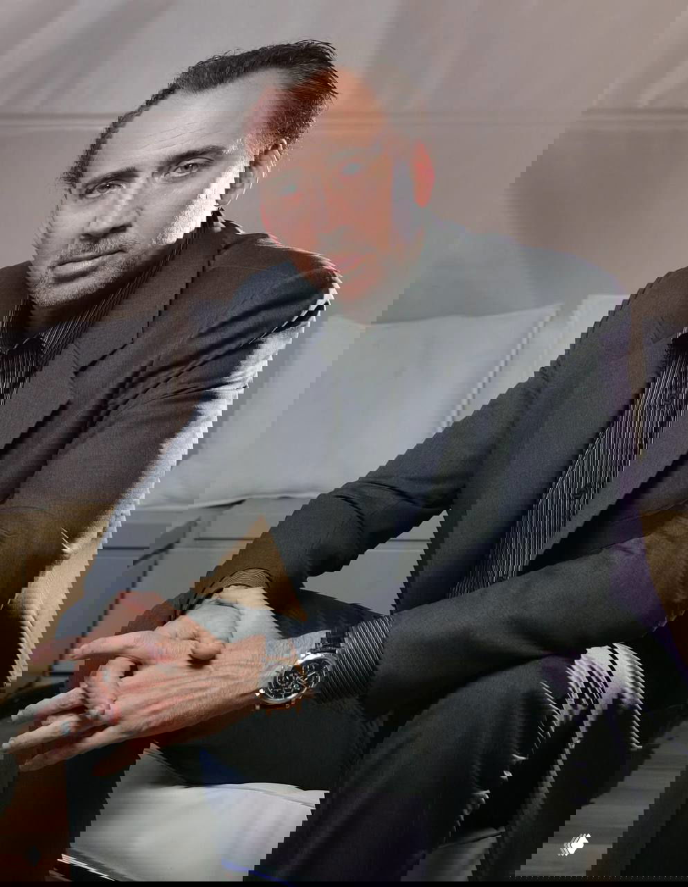 Сидячий портрет в сером костюме: мужчина в официальной позе, скрещенные руки, интерьер в нейтральных тонах.