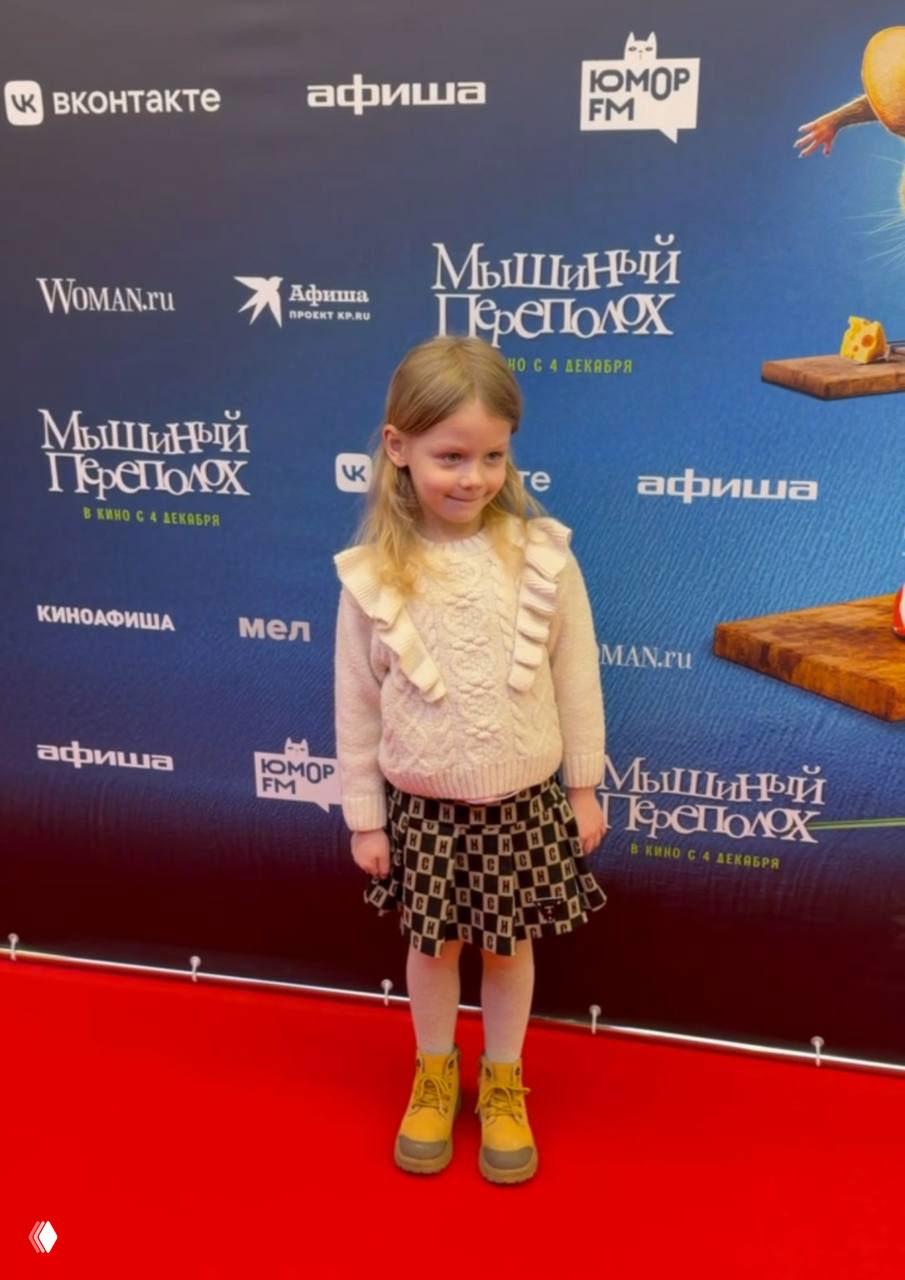 Девочка позирует на красной дорожке на фоне баннера фильма «Мышиный переполох» и логотипов организаторов премьеры.