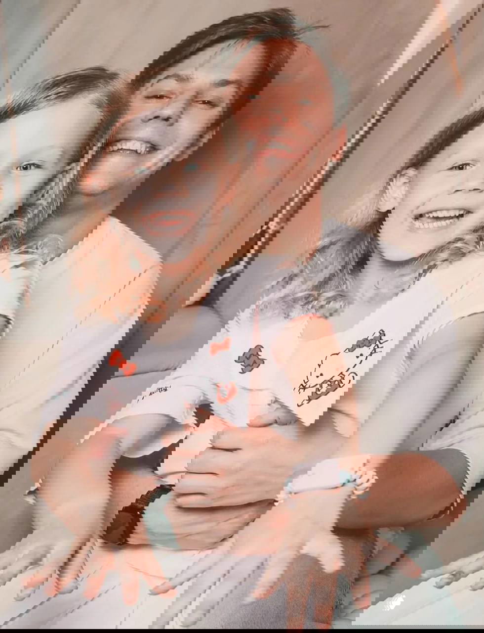 Улыбающаяся девочка сидит у взрослого на коленях в студийной обстановке — тёплое фото с семейной атмосферой, не подписанное именами.