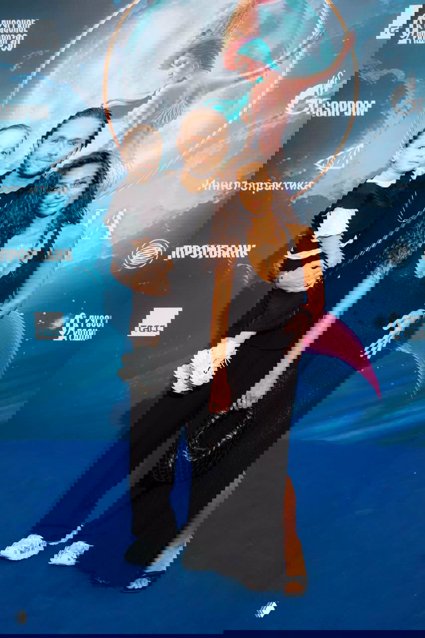 Влад Соколовский, его жена и маленький сын позируют на премьере: семейный снимок на фоне синего баннера с логотипами спонсоров и рекламой.