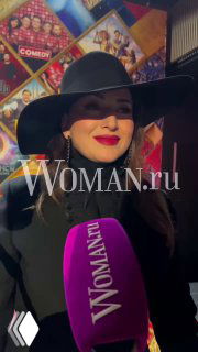 Певица Жасмин в чёрной шляпе на светском мероприятии; крупный план лица с заметным фиолетовым микрофоном Woman.ru на переднем плане, атмосферный портрет.