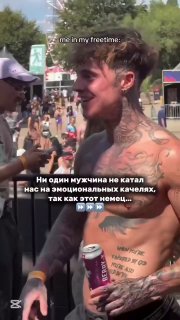 Мужчина без рубашки даёт интервью или общается с камерой на улице среди толпы, летняя атмосферa фестиваля и зрители на заднем плане.