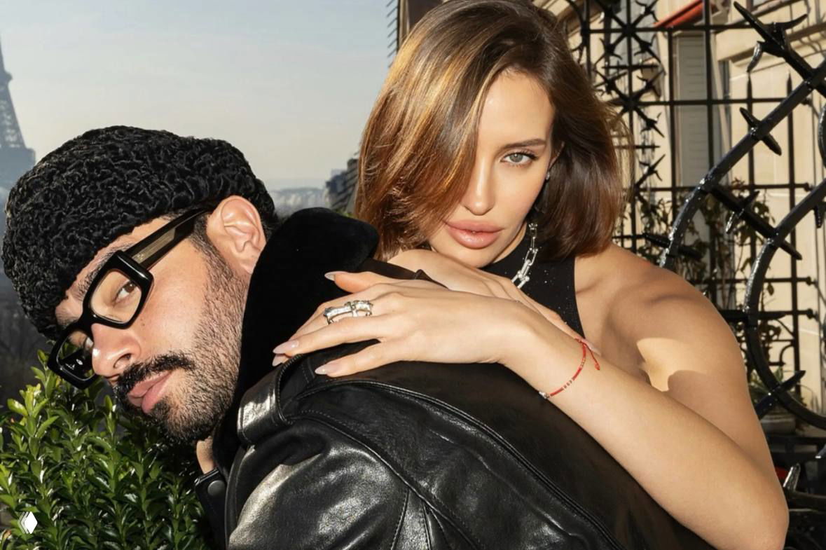 Тимати и Валентина на балконе: мужчина в тёмной шапке и очках обнимает женщину с видимым помолвочным кольцом на фоне городского пейзажа.