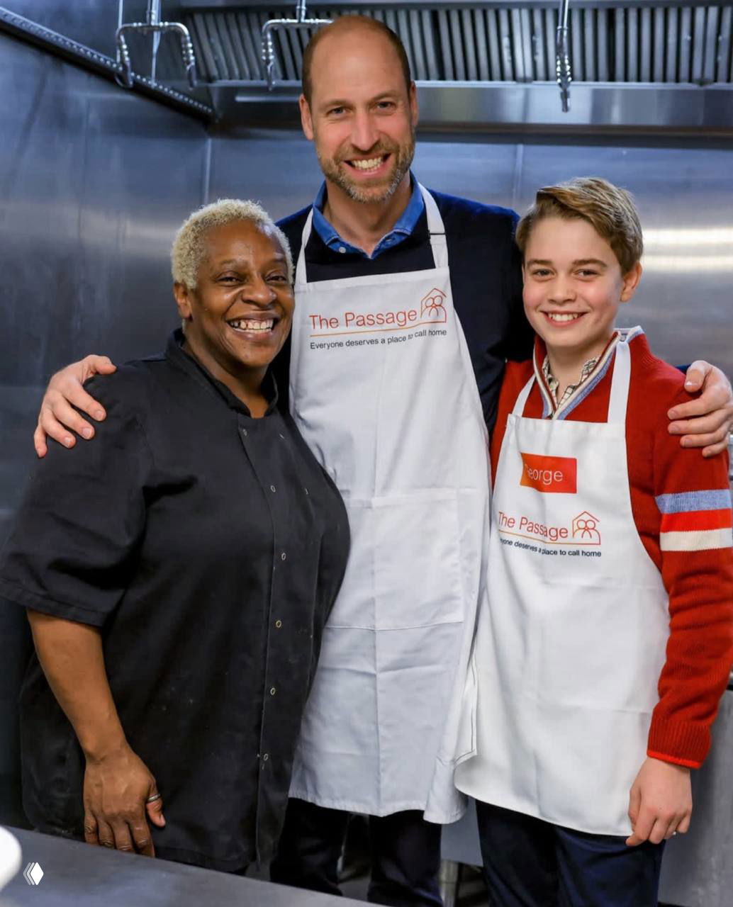 Принц Уильям и принц Джордж в белых фартуках позируют вместе с сотрудницей кухни благотворительного центра The Passage на фоне стального кухонного оборудования.