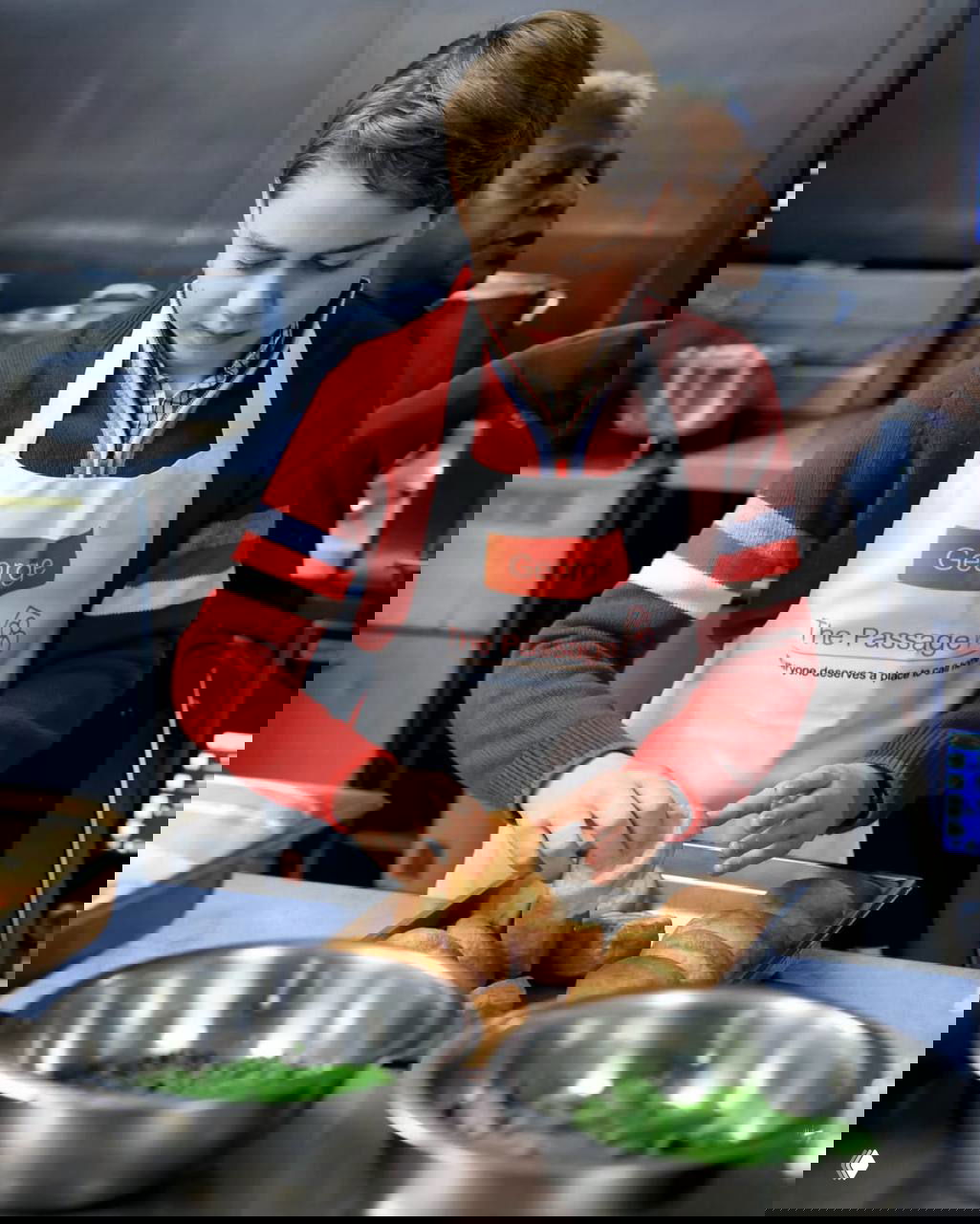 Принц Джордж в красном свитере сосредоточенно раскладывает булочки на подносах на кухонном столе во время благотворительной акции в The Passage.