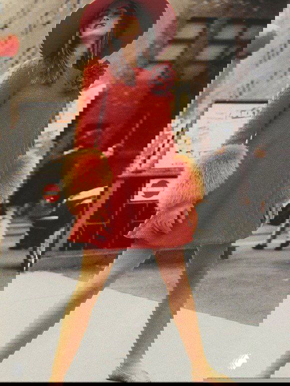 Уличный архивный кадр: модель в красном платье с шляпой и пушистыми манжетами идёт по городу в ярком винтажном образе 1990‑х.