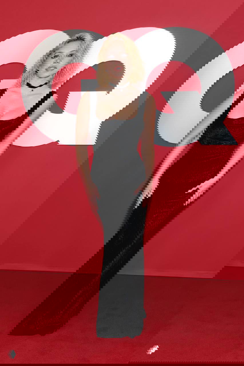 Сидни Суини в чёрном облегающем платье на фоне логотипа GQ, вертикальный кадр с акцентом на силуэт