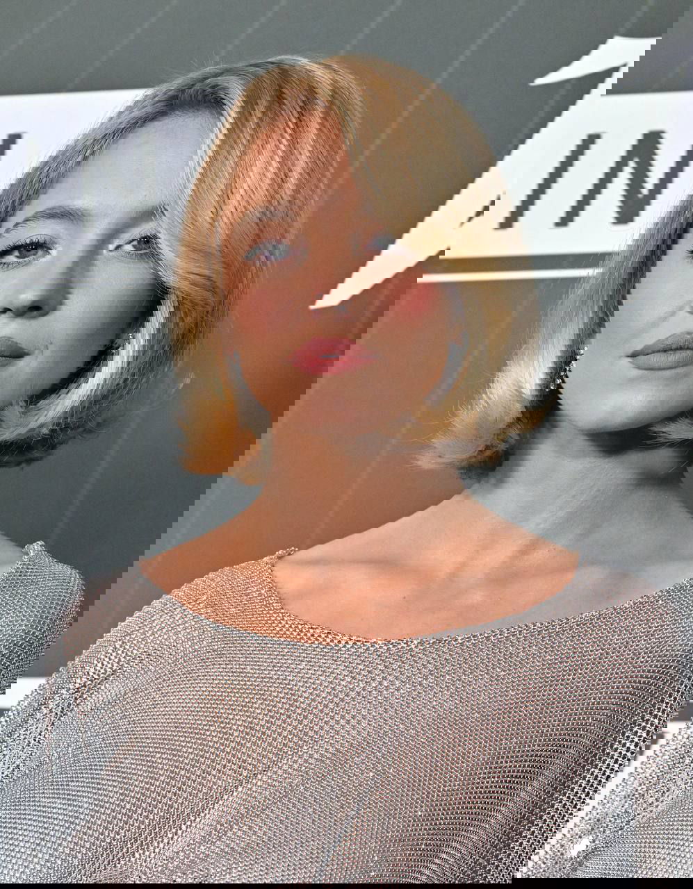 Крупный план женщины с короткой стрижкой каре на светском вечере; аккуратная укладка, нюдовый макияж и серебристое платье на фоне фотозоны.