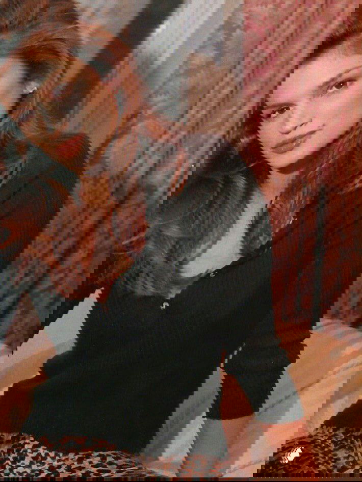 Портретный архивный кадр модели в тёмном пуловере на фоне занавесок, естественный портретный свет, тёплая тональность и ретро‑настроение.