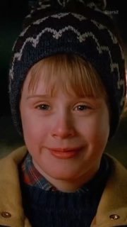 Крупный план мальчика в зимней шапке и пальто: тёплая улыбка и мягкое освещение, кадр передаёт новогоднее настроение фильма.