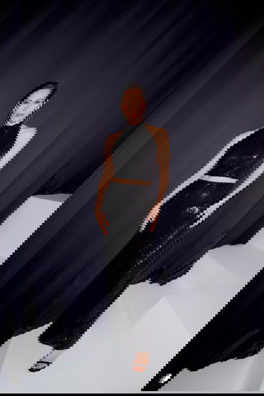 Гостья в чёрном блестящем комплекте позирует на ступеньках и тёмном фоне у фотозоны гала-ужина «Герои PEOPLETALK-2025», вечерний образ.