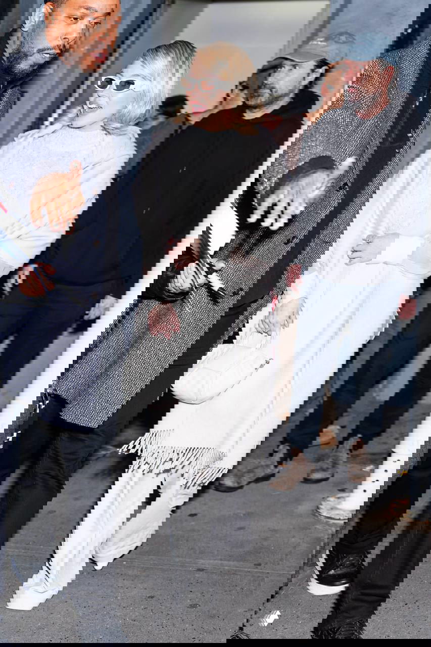 Актриса в светлом пальто и объёмном шарфе, белые брюки и небольшая сумка — повседневный монохромный образ на прогулке