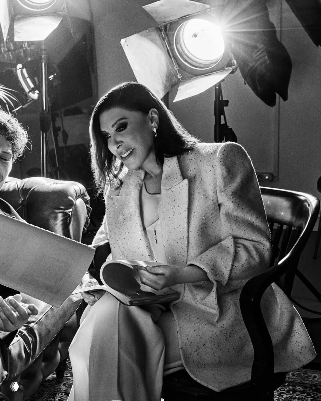 Небахат Чехре в светлом пиджаке перелистывает сценарий под студийными софтбоксами — крупный чёрно‑белый портрет с кинематографичным светом.