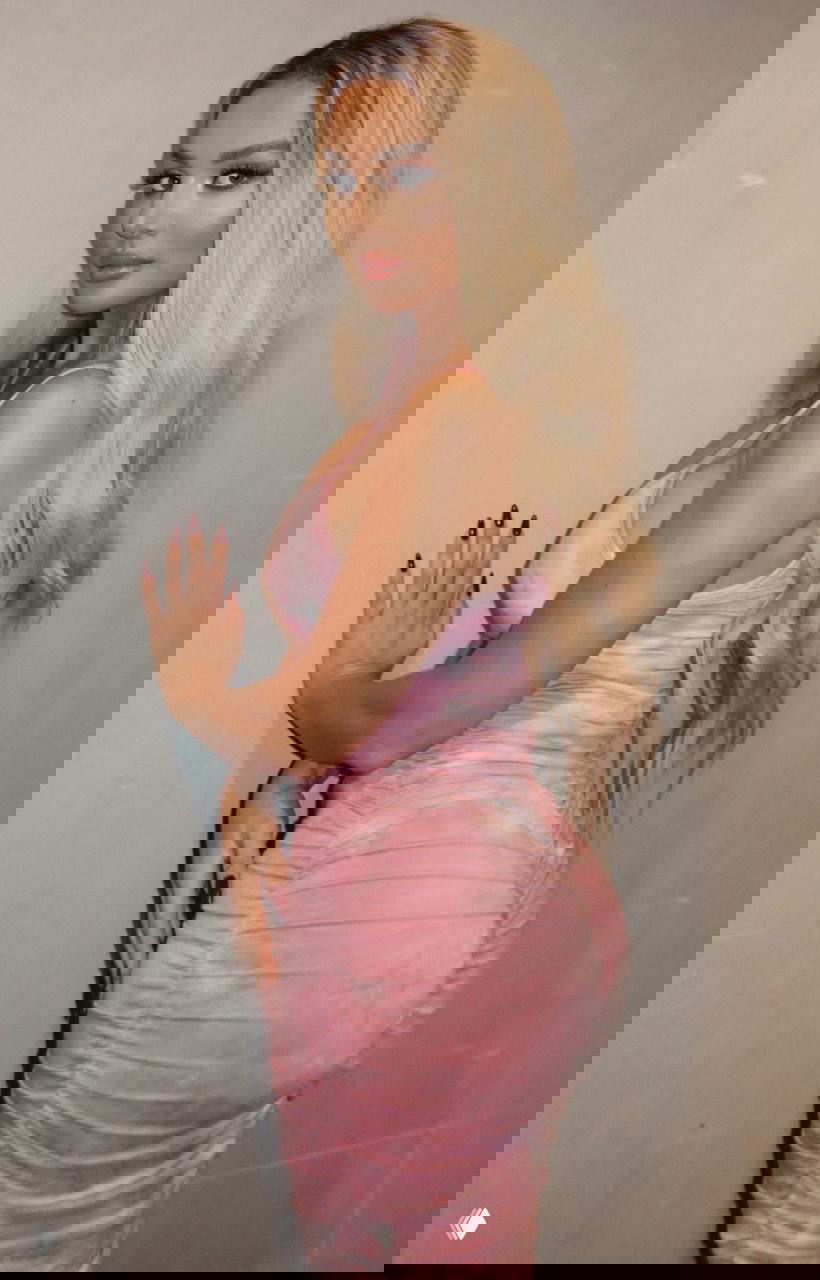 Анна Седокова в розовом облегающем платье в профиль, полный рост; видно причёску, макияж и силуэт на нейтральном фоне.