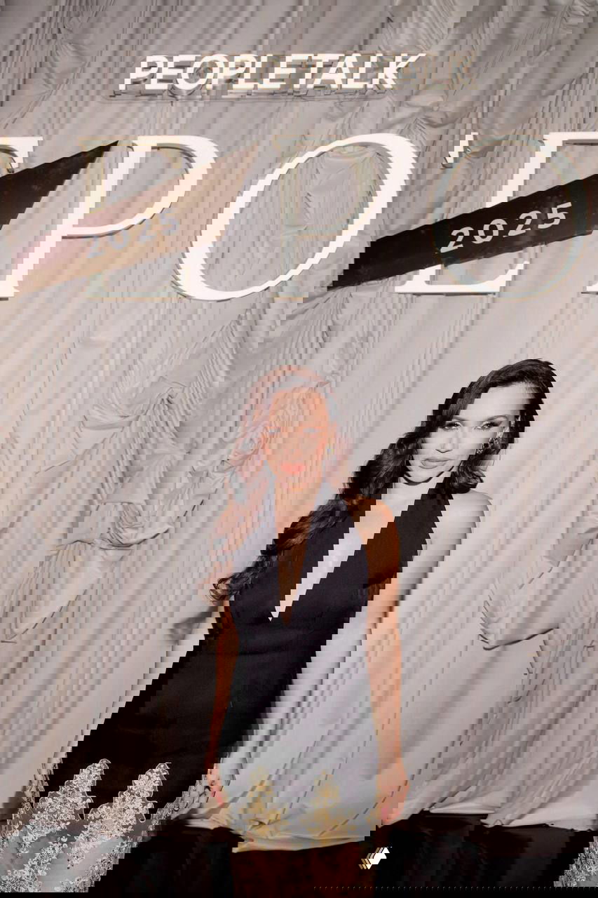 Женщина в чёрном платье с кружевной вставкой и глубоким декольте позирует у оформления сцены с надписью PEOPLETALK 2025 — образ для гала-ужина.