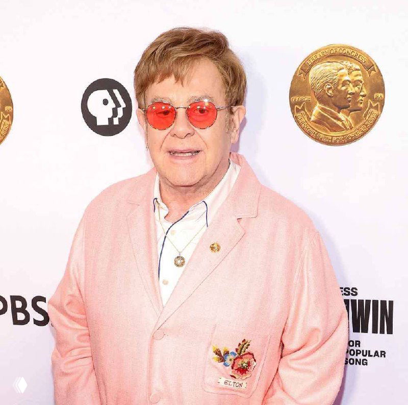 Портрет Элтона Джона в солнцезащитных очках и светлом пиджаке на фоне декоративных графических элементов; изображение искажено цифровыми артефактами.