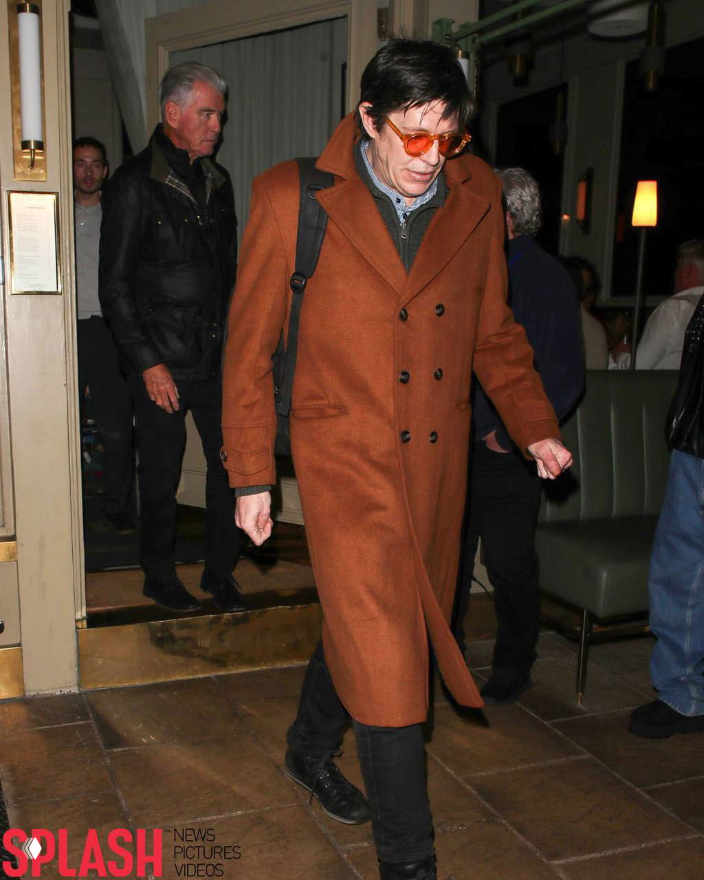 Пирс Броснан в коричневом пальто идёт по входу ресторана в Лондоне: папарацци сделали снимок выхода после совместного ужина.
