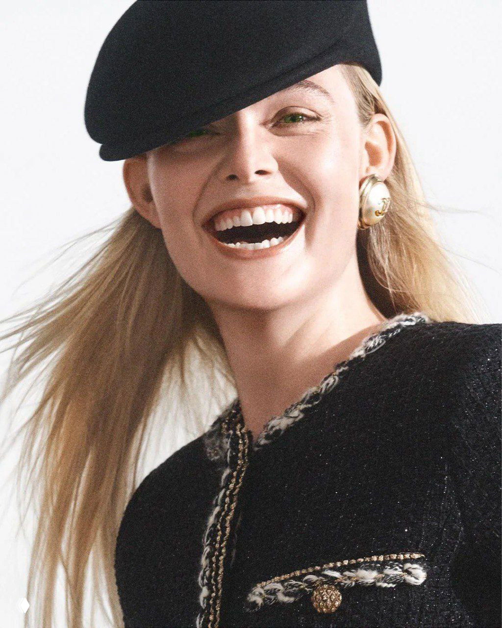 Крупный план улыбающейся женщины-модели в черном берете и украшении — студийный портретный кадр из модной съемки на фоне светлого фона.