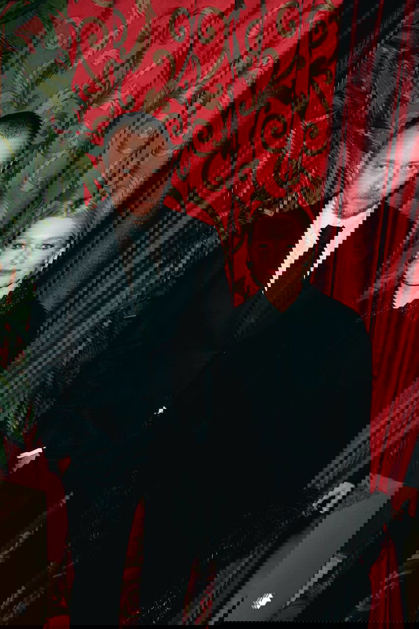 Мужчина в чёрном костюме и женщина в светлой блузе с бордовой юбкой позируют у рождественских украшений — кадр с вечера, видна праздничная инсталляция.