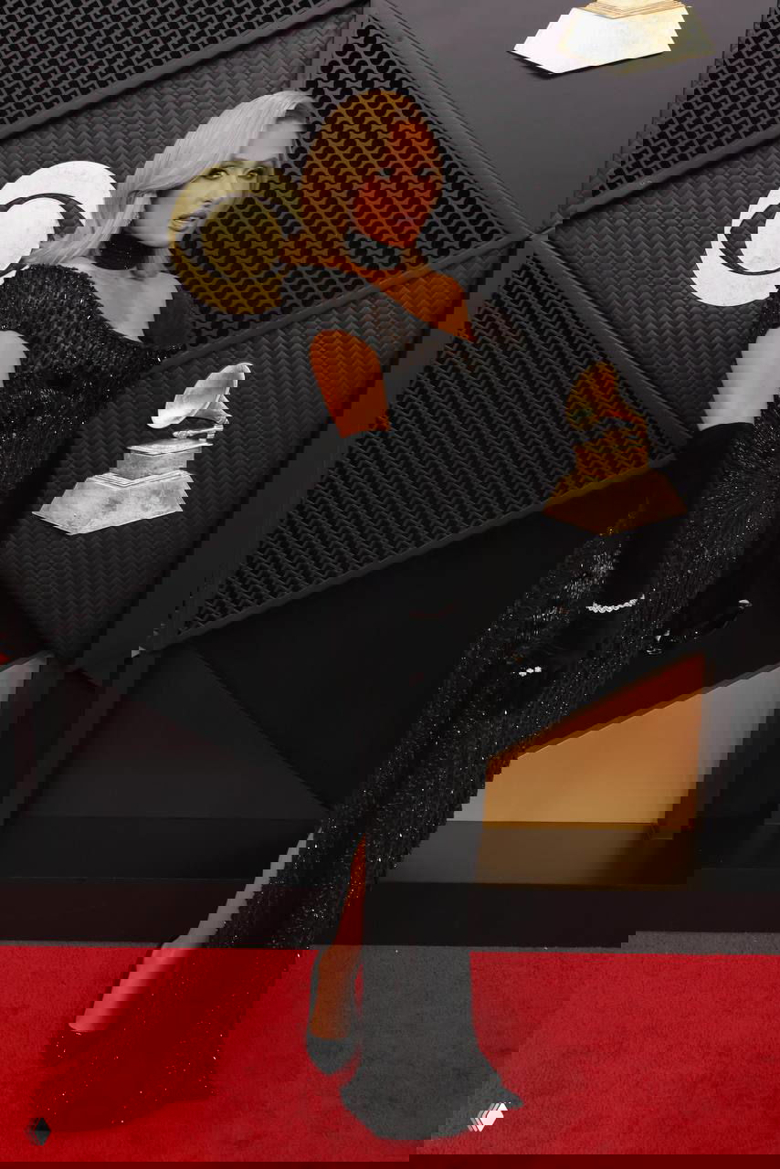 Пэрис Хилтон в элегантном чёрном платье и перчатках на красной дорожке «Грэмми — 2026», на фоне фирменного декора премии.