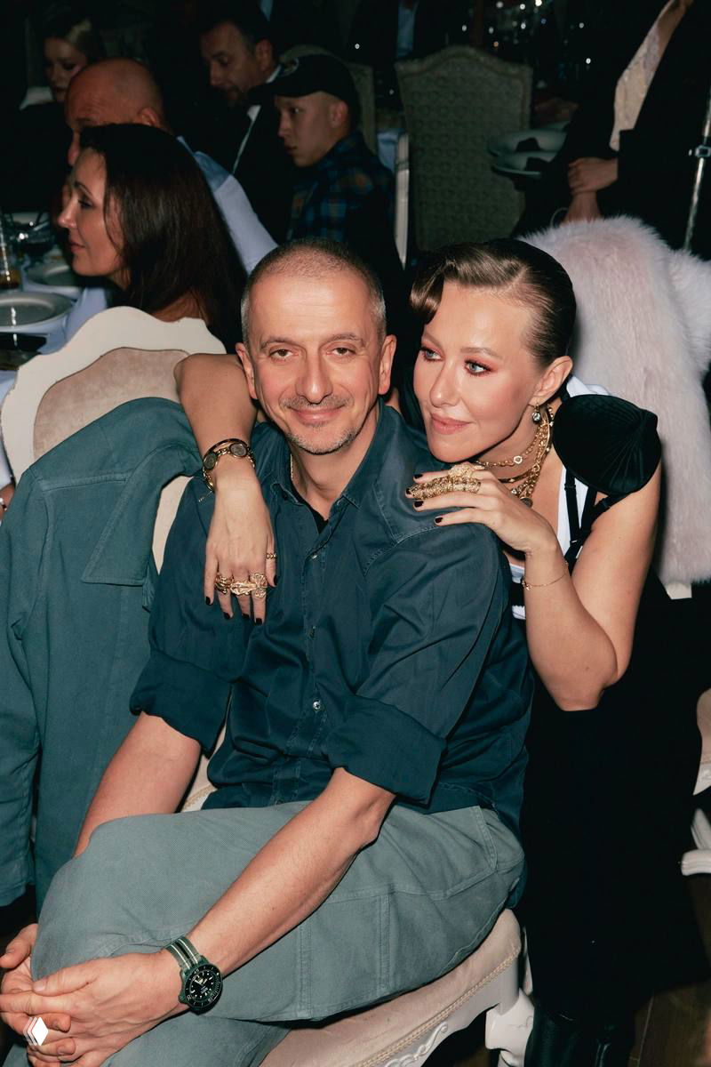 Мужчина и женщина в чёрной одежде позируют у красных портьер: кадр из фотозоны благотворительного вечера, спокойная и тёплая композиция.