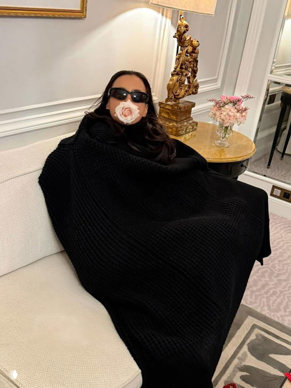 Интерьерный кадр: человек в темной одежде лежит на диване в роскошном номере отеля, рядом вазочка с розами и декоративная лампа.