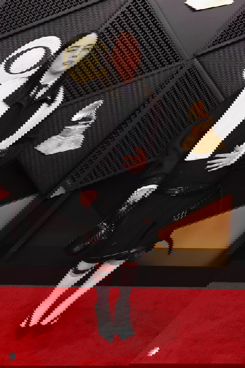 Билли Айлиш в чёрно‑белом неформальном образе с пиджаком, белыми носками и туфлями, позирует на красной дорожке «Грэмми — 2026».