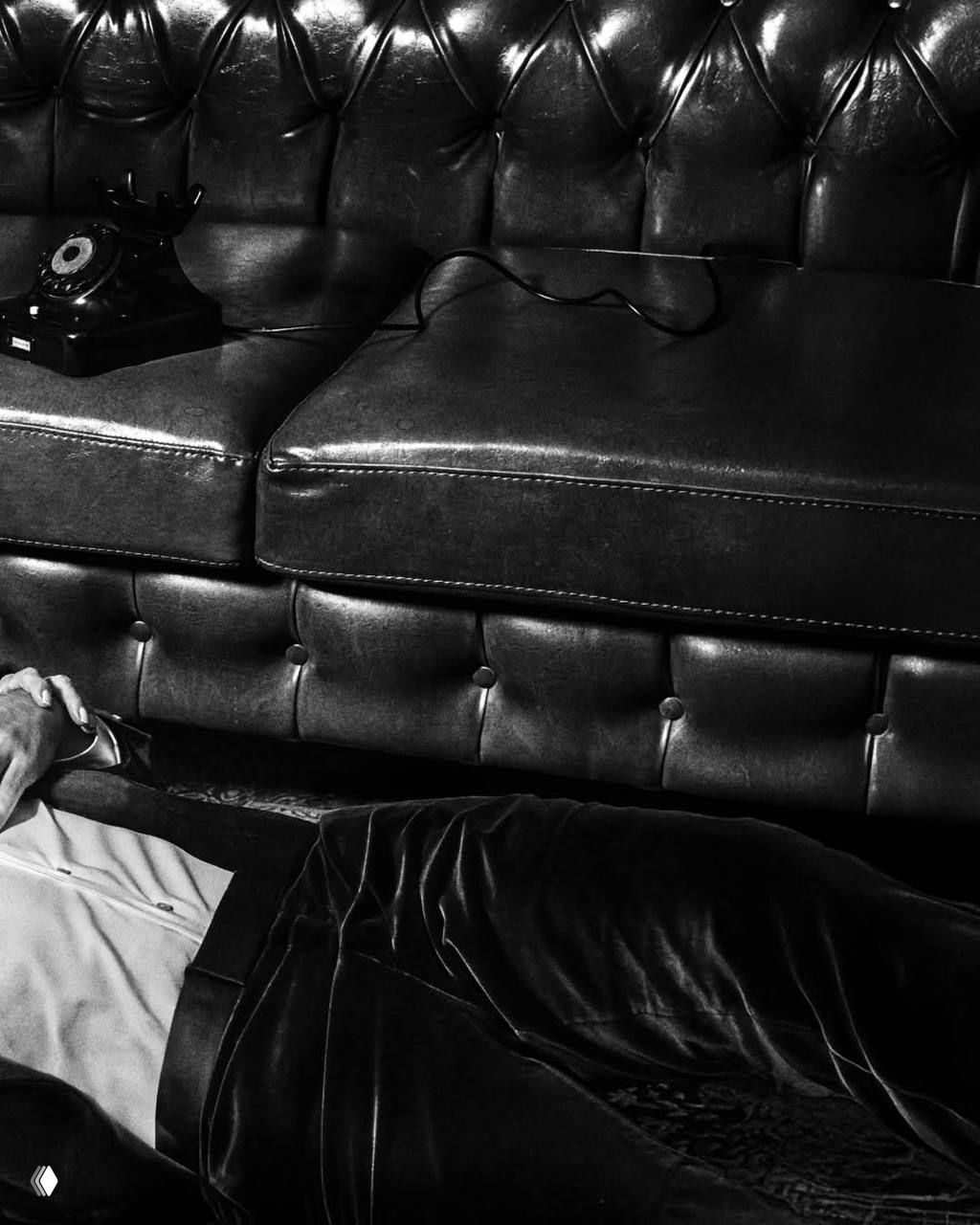 Детали съёмочной студии: ретро‑телефон на диване и фрагмент костюма с лежащим актёром — атмосферная чёрно‑белая композиция с текстурой кожи.