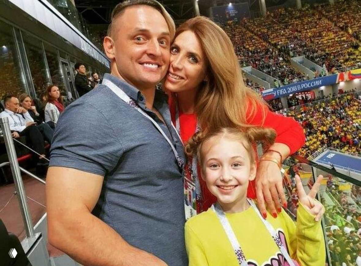 Аскольд Запашный с женой и дочерью Евой на трибуне стадиона — семейное фото во время спортивного мероприятия, улыбающиеся лица на фоне зрителей.